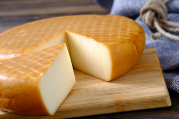 A round smoked cheese on a wooden board, beautifully sliced, ideal for gourmet meals and gatherings.