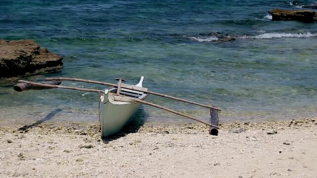 A bangka or Filipino traditional outrigger boat moored in the beach with the ambient motion of waves in a crystal clear sea of Apo Island in Dauin, Philippines