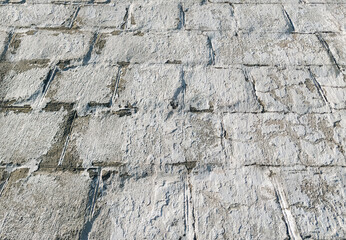 A cracked, light gray, almost white cinder block wall coated with acrylic-based chalk-lime paint. The texture of the old stone surface. Close-up.