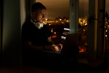 A young male developer is programming a code script late at night with beautiful city lights at night.