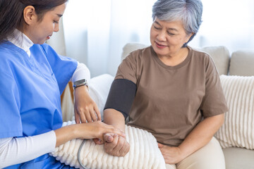 Obraz premium Asian caregiver nurse assisting elderly senior woman at home during medical checkup, measuring blood pressure and providing healthcare support, doctor visit and homecare service concept