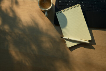 Above office desk notebook with pen and coffee with laptop on wooden desk soft morning sunlight
