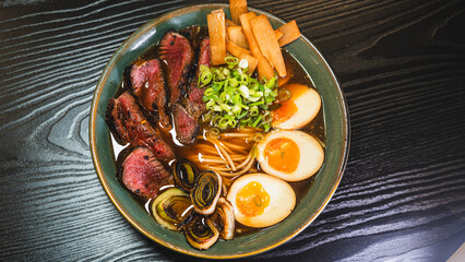 Succulent rare beef ramen in a beautiful bowl with bamboo shoots, spring onions, tamago (Japanese marinated egg), and leeks. Rich broth, authentic Japanese flavors.