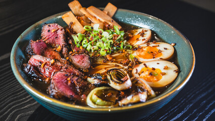 Succulent rare beef ramen in a beautiful bowl with bamboo shoots, spring onions, tamago (Japanese marinated egg), and leeks. Rich broth, authentic Japanese flavors.