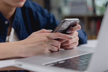Woman hand using smartphone typing, work home office desk laptop. Business technology concept, online communication, social media, multitasking. Remote work, check email, app, browsing internet.