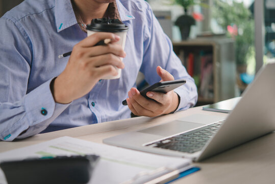 Man hand smartphone coffee cup, work home office desk. Multitasking business, remote work. Check online data, browsing internet, freelancer lifestyle concept. Financial analysis document calculator.