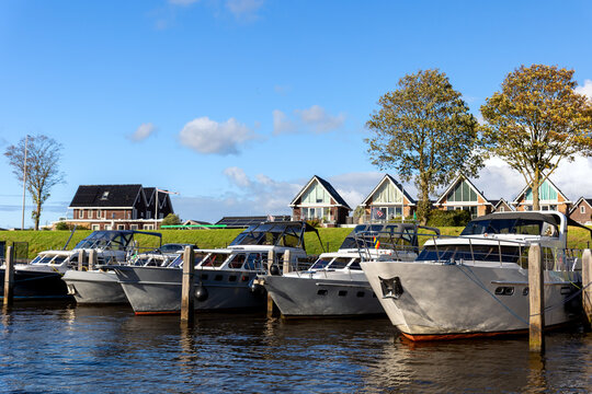 Modern luxury boats moored at Zwartsluis Netherlands canal marina bright sunlight modern houses trees background. Calm water reflects the vessels and blue sky, creating a serene Dutch coastal scene