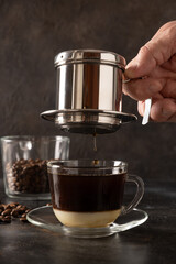 Brew Vietnamese coffee with sweet condensed milk in glass cup by traditional method on black background. Close up.