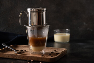 Traditional method of making Vietnamese coffee with sweet condensed milk in glass cup on black background. Close up.