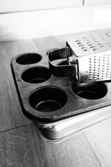 Black and white close-up of essential kitchen tools a classic metal muffin pan and a versatile box grater, ready for baking or culinary tasks, with a rustic, timeless aesthetic