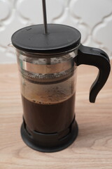 Aromatic dark coffee steeping in a classic glass French press, resting on a warm wooden surface, embodying the simple pleasure of a freshly brewed morning or afternoon beverage