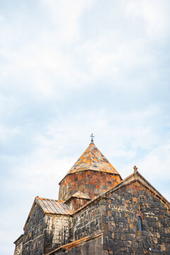 Close-up of the Sevanavank Monastery, a historic Armenian church built with volcanic basalt and tuff stones, featuring an orange-tiled dome topped with a cross.