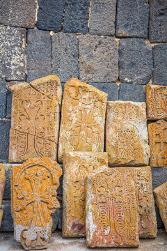 Close-up of traditional Armenian khachkars (carved cross-stones) displayed against a basalt wall at Sevanavank Monastery in Armenia. The ornate crosses and floral motifs, represent centuries