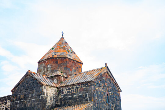 Beautiful close-up of Sevanavank Monastery, an ancient Armenian church built with dark basalt and orange tuff stones, standing majestically under a clear blue sky