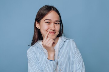 A young woman smiling playfully against a blue background, wearing a striped shirt, with long hair and a casual pose
