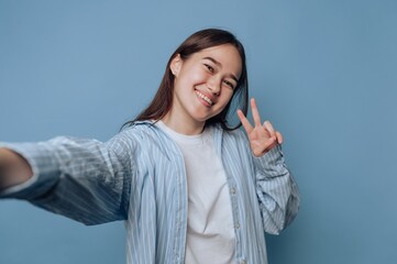 Young woman taking a selfie with a peace sign on a blue background.