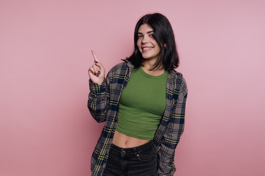 Smiling woman pointing upwards against a pink background.