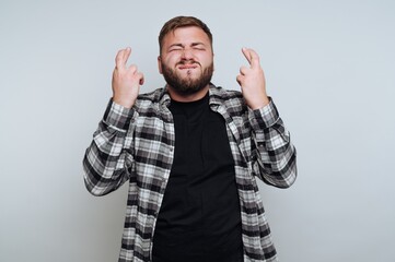 Naklejka premium Man with beard crossing fingers, wearing plaid shirt, hopeful expression.