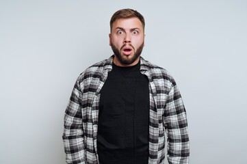A surprised man with a beard wearing a plaid shirt and black t-shirt.