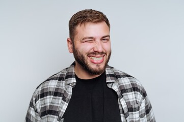 Smiling man winking, wearing a plaid shirt against a plain background.