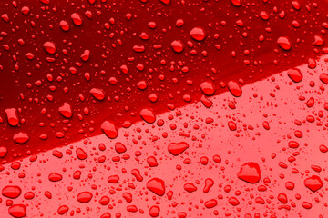 Water droplets on a glossy red surface creating a vivid abstract pattern with strong reflections and contrast. Perfect for backgrounds or modern design concepts