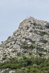 Fototapeta premium Rocky mountain peak with cross and small chapel surrounded by greenery in Crete