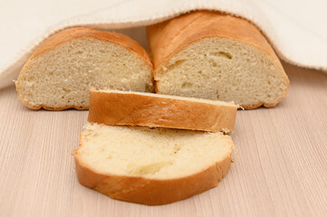 A delicious crispy loaf of bread under a white towel on a wooden table.