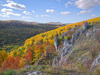 Vibrant autumn colors around the rocky cliffs of Köpüs-kő in the Bükk Mountains, Hungary, with bright foliage and scenic mountain slopes under blue skies.