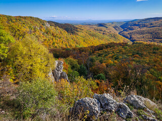 Panoramic autumn view from Köpüs-kő in the Bükk Mountains, Hungary, looking toward the Garadna Valley and distant Tokaji Hills under a clear blue sky.