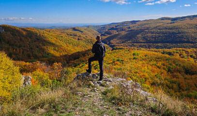 A hiker stands on the edge of Köpüs-kő in the Bükk Mountains, gazing over the colorful autumn forests and valleys of northern Hungary.