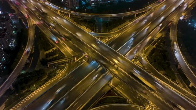 Aerial view of cars blurring on a busy highway intersection at night, city background. Transportation