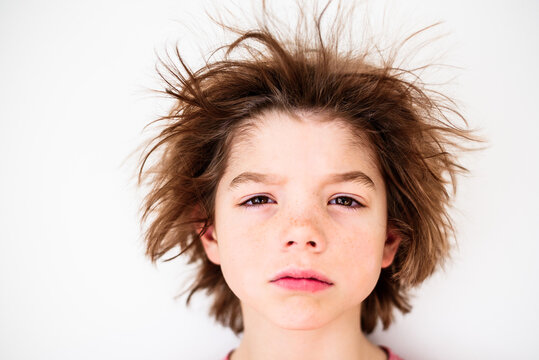 Portrait of a tired boy with freckles and messy brown hair in front of a white background