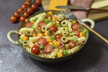 Durum wheat semolina pasta salad made with peppered salami cherry vine tomatoes red leicester cheese green pitted olives and spring onions.