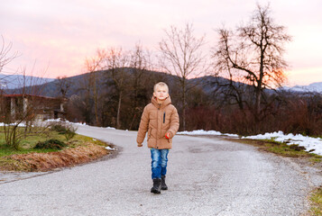 Fototapeta premium Caucasian boy walking on country road at sunset in winter landscape