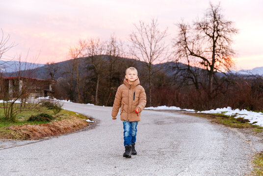 Caucasian boy walking on country road at sunset in winter landscape