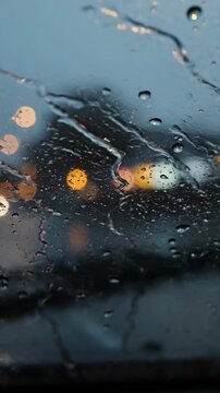 Raindrop patterns on glass window blur city lights creating wet, moody atmosphere with reflective water and soft evening light during rain