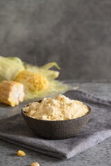 Organic Cornmeal in Gray Bowl with Fresh Corn Cobs on gray background. Close up.