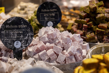 A close-up of a vibrant display of pink, powdered passionfruit flavored turkish delight (halkum) cubes, next to other varieties, for sale in the Mahane Yehuda Market.