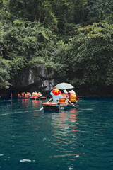 Tourists wearing life vests and traditional hats are enjoying a peaceful scenic boat ride through the lush jungle landscape in tam coc, ninh binh, vietnam © Fotografia Juan Reig
