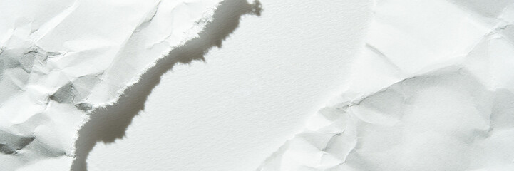 Close-up of torn white paper with creased texture and shadows on light background.