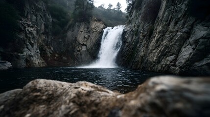 Fototapeta premium A powerful waterfall cascades into a dark pool surrounded by rugged cliffs and natural elements under an overcast sky
