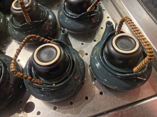 Small, dark blue-green ceramic teapots with wicker handles, each topped with a matching teacup....