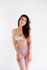 Obraz premium Sports sexy woman standing in activewear with abs muscles looking at camera isolated on white background. Caucasian 30s fitness girl wears beige top pink leggings. Slim fit smiling brunette blue eyes.