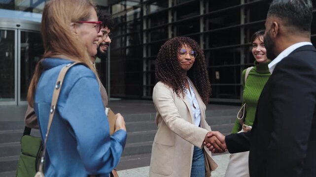 African American female business woman shaking hands with company partner in front of modern office buildings 
