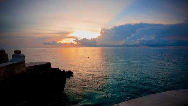 Stunning cloudscape serene quiet tranquil ocean wall sunset with gentle waves lapping against ocean wall with a solitary swimmer off in the distance.
