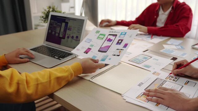 Excellent startup company employee presenting user interface prototype for mobile application to smart co-worker in office workspace. UX UI designer explain function of icon design on paper. Synergic