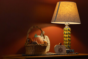 Photo of a Table and lamp showing a warm fall scene with pumpkins and a basket and a red background