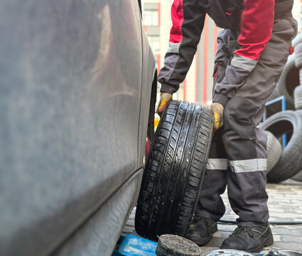 An African-American tire fitter with a wrench in his hands while working. The tire fitter removes the tire from the car. Mechanic changing a car tire on a vehicle a hoist using an pneumatic drill.  - Powered by Adobe