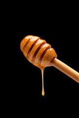 Honey dripping from honey dipper  on black  background