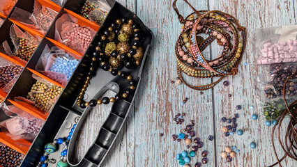 Plastic bead box with colorful beads and bracelets on the wooden table. 